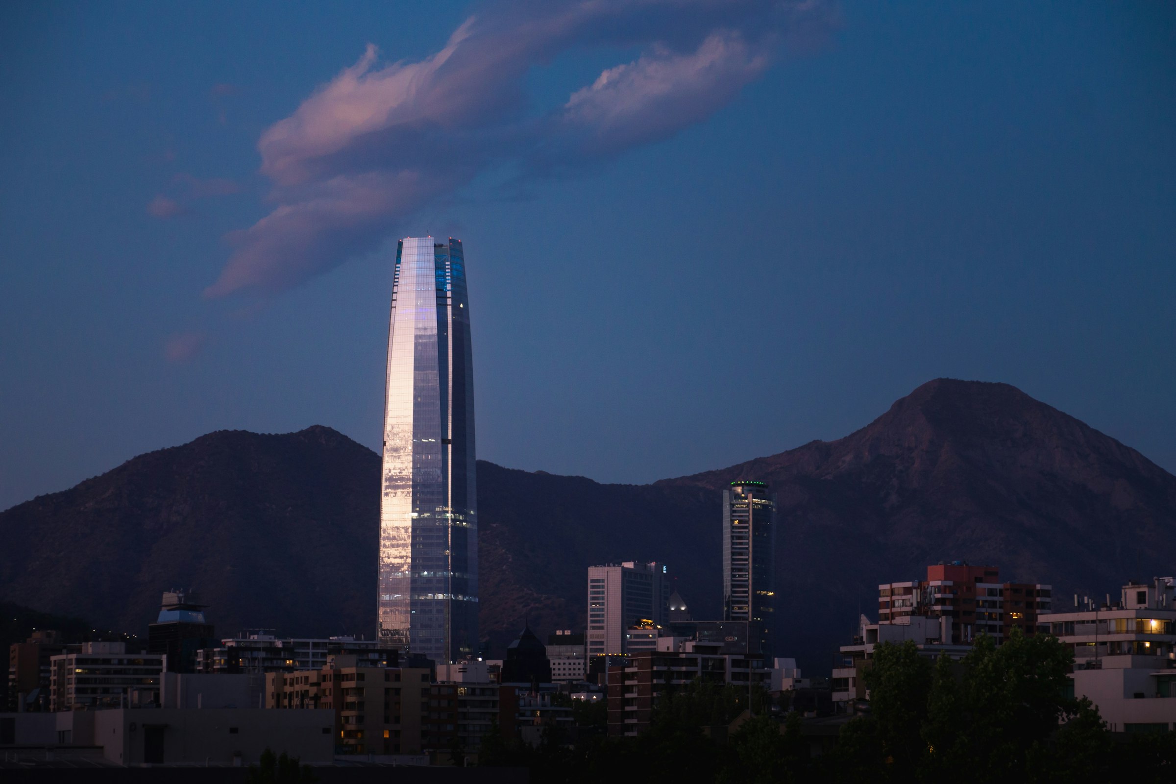 La torre Costanera y los cerros de Santiago al anochecer, bajo una nube rosada.